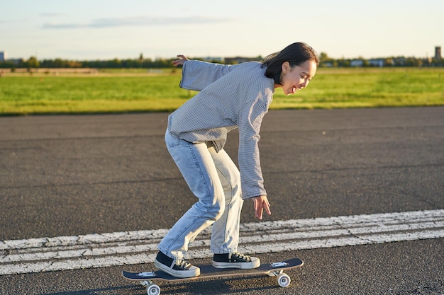Foto gratuita felice ragazza skater in sella al suo skateboard e divertirsi sulla strada vuota donna sorridente che si gode la crociera