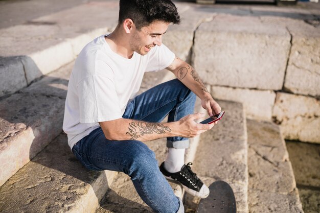 Счастливый фигурист, играющий на смартфоне, сидящий на ступеньках