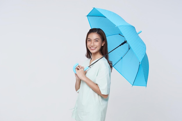 흰색 배경 생명 보험 및 보호 개념에 고립된 파란 우산을 들고 서서 행복한 미소를 짓는 아시아 여성