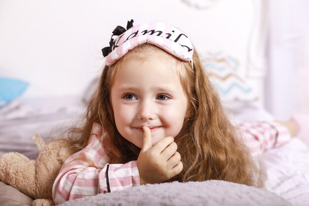 행복한 미소 빨간 머리 소녀 아이는 거대한 침대에서 침대 시트에 누워있다