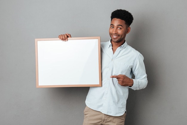 Free photo happy smiling african man pointing finger at blank board