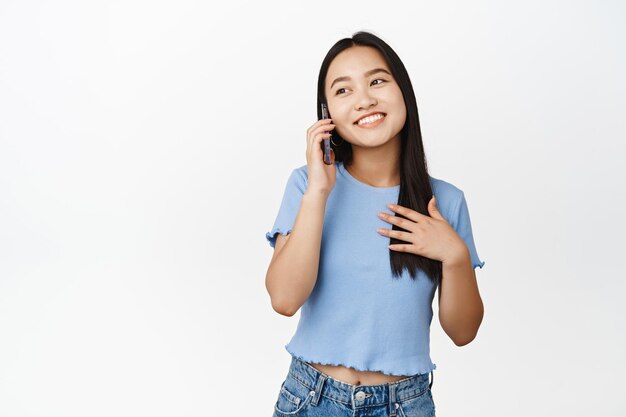 흰색 배경 복사 공간 위에 서 있는 휴대폰으로 통화하는 행복한 미소 아시아 소녀 응답 전화