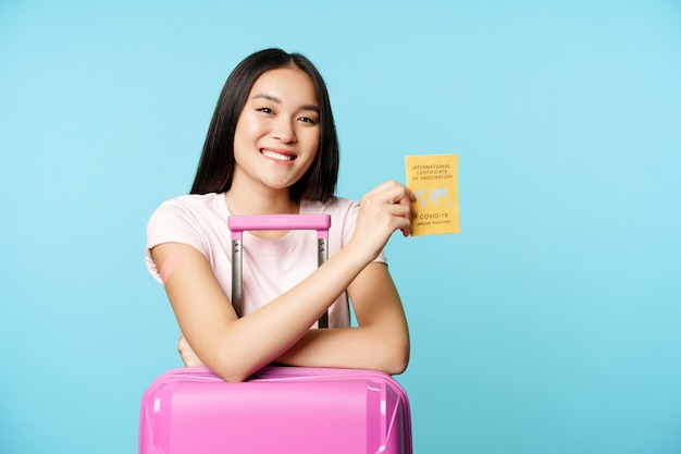 Happy Smiling Asian Girl Tourist Stands With Cute Suitcase In Airport Shows International Covid Vacc...