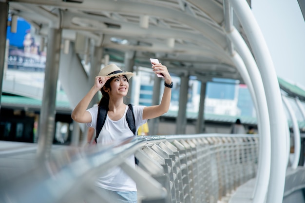 Foto gratuita ragazza asiatica sorridente felice dello studente con lo zaino al fondo della città