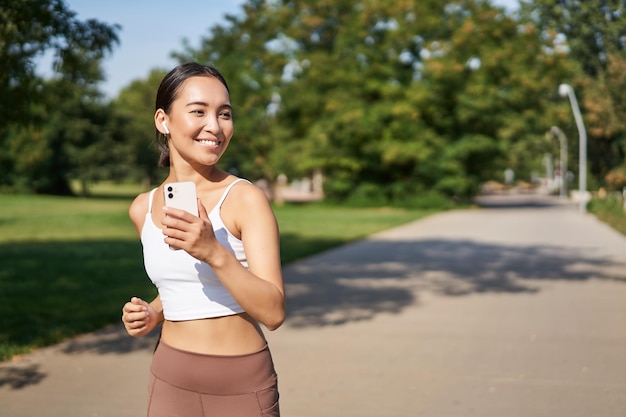 Happy smiling asian woman jogging in park healthy young female runner doing workout outdoors running