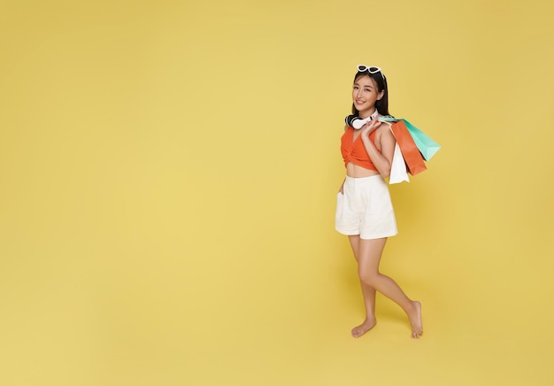 여름 드레스 를 입고 쇼핑 가방 을 들고 있는 행복 한 미소 짓는 매력적 인 아시아 여성