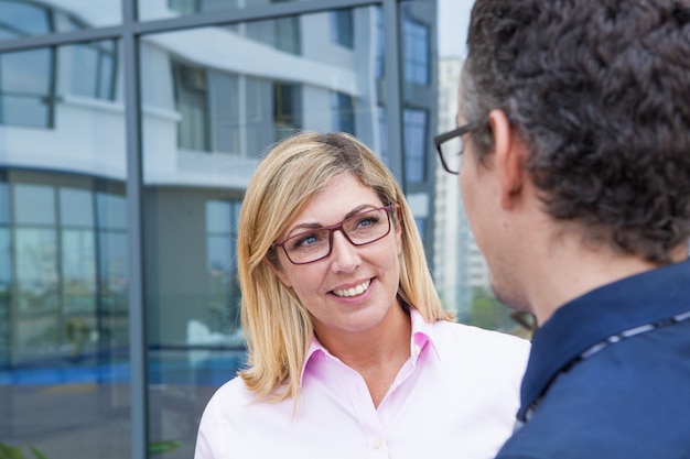 Happy smiling attractive businesswoman in eyeglasses talking to colleague outdoors.