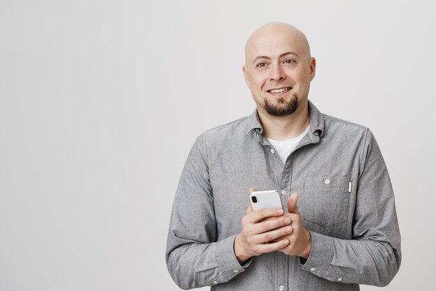 Happy smiling bald adult man look aside, holding smartphone
