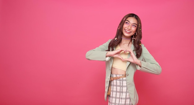 Free photo happy smiling beautiful asian teen woman standing showing heart sign isolated on pink copy space background lifestyle people emotions and casual concept