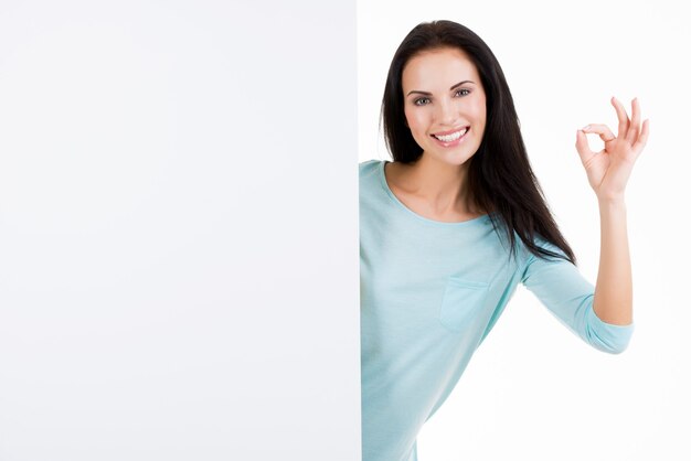 白で隔離の空白の看板を示す幸せな笑顔の美しい若い女性