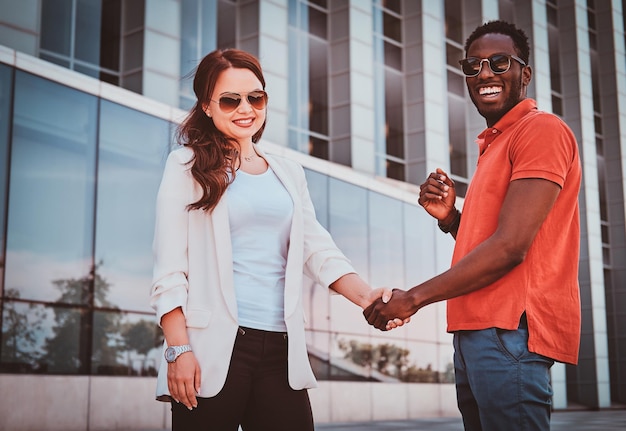 Happy smiling bisness partners in sunglasses meeteng up near glass building at city centre.