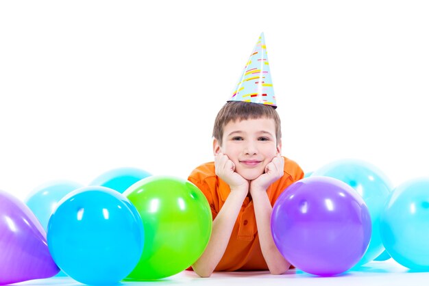 Happy smiling boy in orange t-shirt lying on the floor with colorful balloons and showing thumbs up - isolated on a white