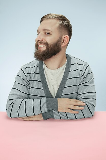 happy and smiling business man sitting at table on blue studio background. portrait in minimalism style