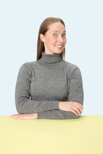 The happy and smiling business woman sitting at table on a pink studio background. The portrait in minimalism style