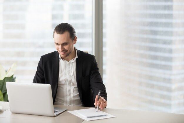 Happy smiling businessman in office looking at laptop sreen.