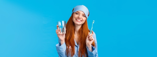 Free photo happy smiling and carefree redhead enthusiastic girl in sleep mask pyjama holding glass water and to