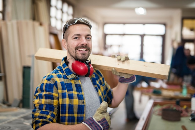 Free photo happy smiling carpenter holding wood material and thumbs up in his carpentry workshop