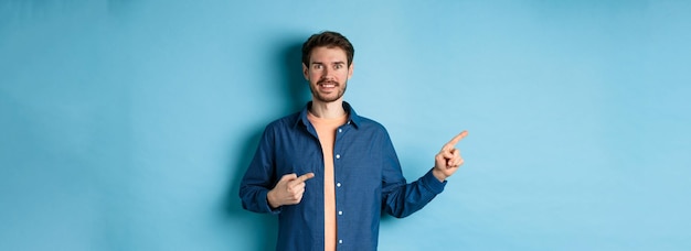 Free photo happy smiling caucasian man showing advertisement pointing fingers left at empty space standing on b