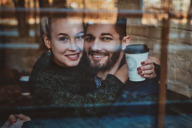 Happy smiling couple is sitting in cafe and looking through the window while enjoying their coffee.