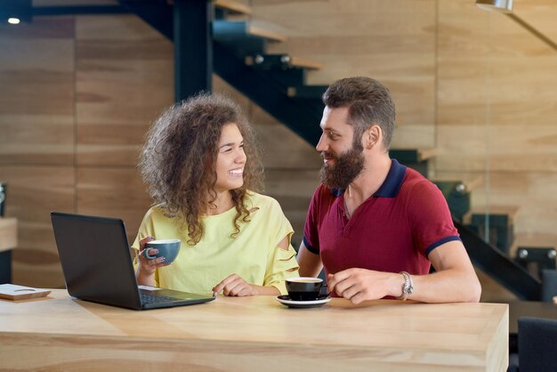 Счастливая улыбающаяся пара смотрит друг на друга и пьет кофе в кафе