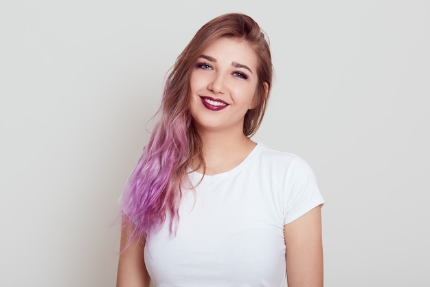 Happy smiling female dresses casual attire having lilac hair  girl with pleasant appearance being in good mood, posing isolated over gray wall.