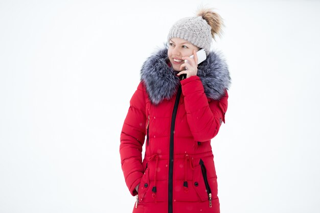 Счастливый улыбается женщина в красной зимней куртке разговаривает по мобильному телефону, на улице, против снега