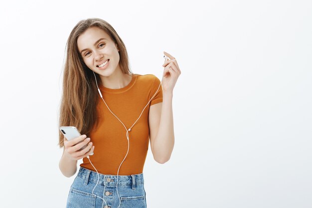 Happy smiling girl take-off headphone and looking, listen podcast or music on mobile phone