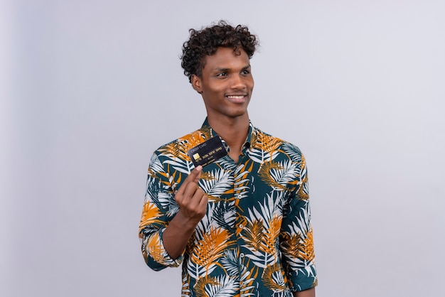 Free photo happy and smiling good-looking dark-skinned man with curly hair in leaves printed shirt showing credit card