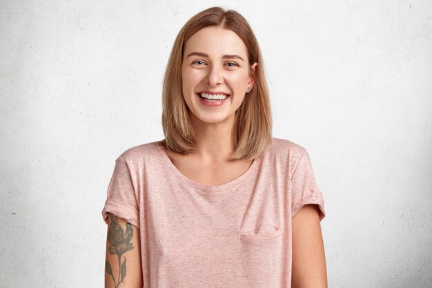 happy smiling good looking young female with positive smile poses indoor against blank copy space, expresses happiness
