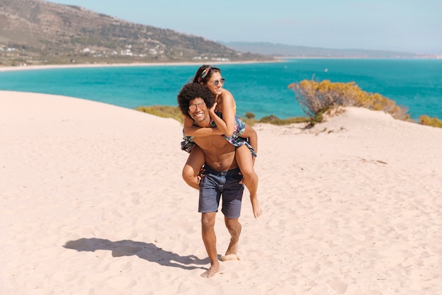 幸せと笑顔の男がビーチで女の子を背負って