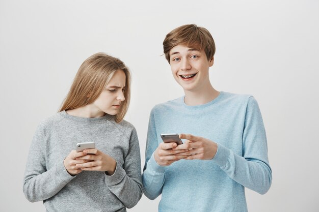 Happy smiling guy with braces laughing over funny message, girl peeking his mobile phone screen