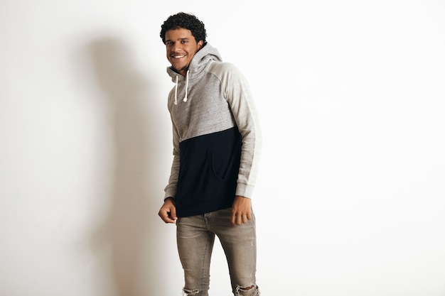 Happy smiling latino guy wears blank grey black sweater with hood and distressed jeans, isolated on white