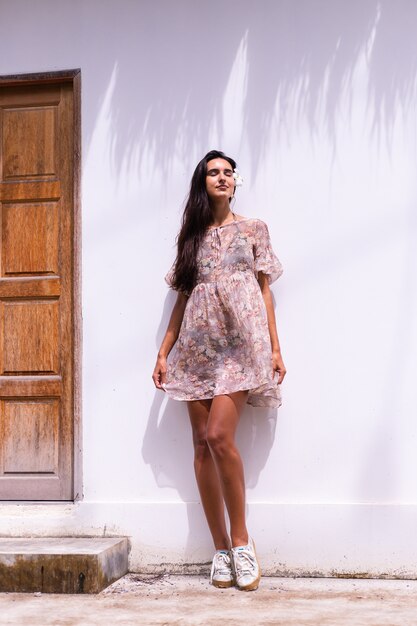 Happy smiling long haired woman in dress stands on white wall