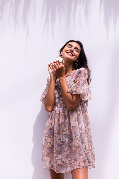 Happy smiling long haired woman in dress stands on white wall