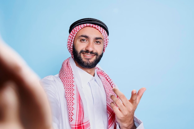 無料写真 伝統的なイスラム教徒の服を着た幸せな笑顔の男性がビデオコンファレンス fpvでチャットし ⁇ スマートフォンを手に持ってカメラを見ている陽気なアラブ人