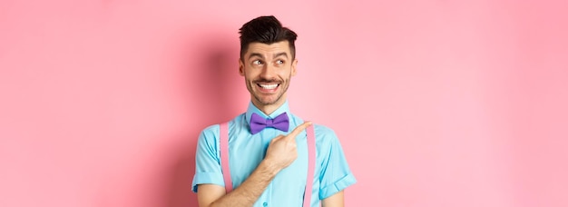 Free photo happy smiling man in funny outfit and bowtie pointing finger left and looking at logo showing advert