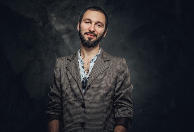 Happy smiling man with amulet on the neck is posing for photographer at dark photo studio.