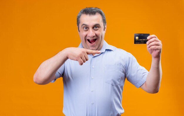 Счастливый и улыбающийся мужчина средних лет в синей рубашке с вертикальной полоской, указывая указательным пальцем кредитной карты