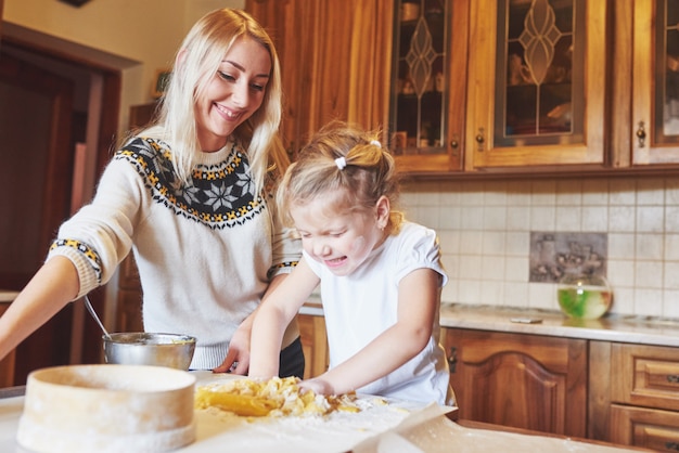 Happy smiling mom in the kitchen bakes cookies with her daughter.