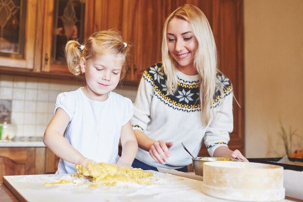 Счастливая улыбающаяся мама на кухне печет печенье с дочерью.