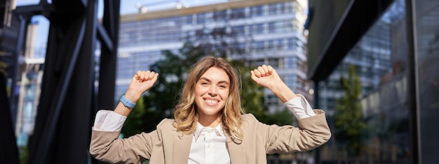 Happy smiling saleswoman in beige suit celebrates her achievement triumphing making fist pump and