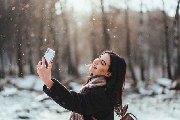 ウィンターパークでスマートフォンでselfieを取っている幸せな笑顔の10代の少女または若い女性
