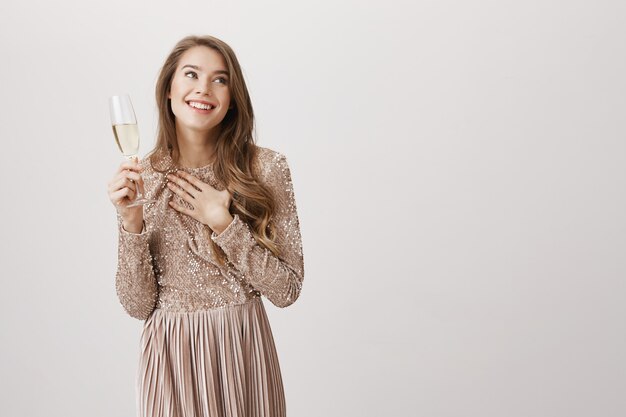 Счастливая улыбающаяся женщина в вечернем платье пьет шампанское