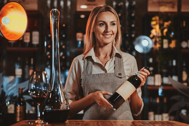 Happy smiling woman is prepairing wine for sommelier to expertise it at wine boutique.