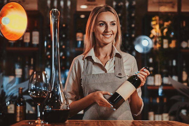 Happy smiling woman is prepairing wine for sommelier to expertise it at wine boutique.