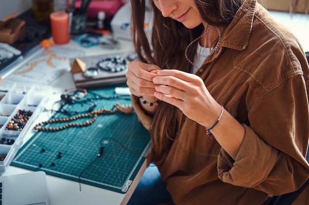 Free photo happy smiling woman is working on beads jewellery at her own workplace.