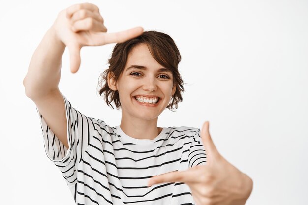 Счастливая улыбающаяся женщина просматривает ручные рамки, фотографирует, стоит на белом фоне