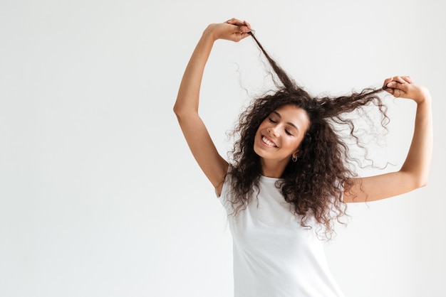 Foto gratuita donna sorridente felice che gioca con i suoi lunghi capelli ricci