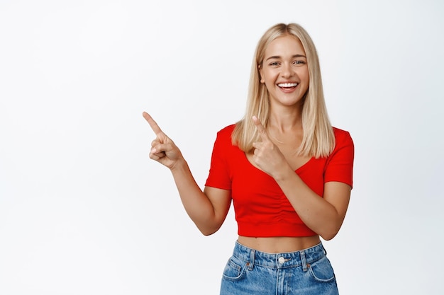 白い背景の上に立っている広告やロゴを示す左上隅に指を指している幸せな笑顔の女性