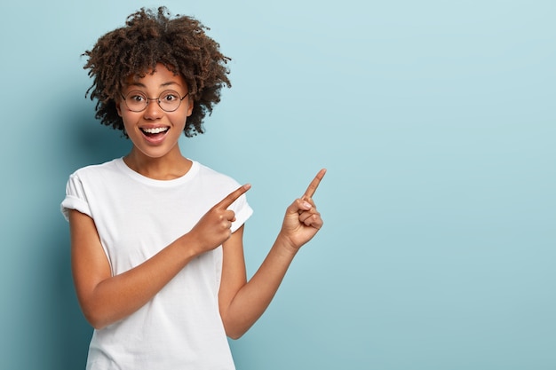 Foto gratuita il venditore sorridente felice della donna indica nell'angolo in alto a destra, pubblicizza l'oggetto su uno spazio vuoto, ha un'espressione facciale amichevole